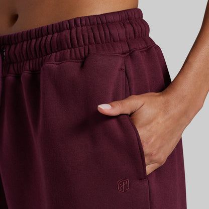 A model wearing wide-leg lounge pants in deep burgundy, with hand in side pocket.