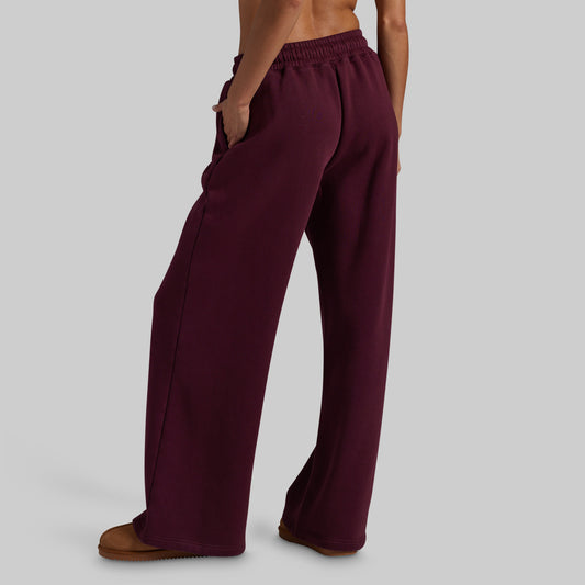 A model wearing wide-leg lounge pants in deep burgundy, paired with brown suede slippers, shown from behind.