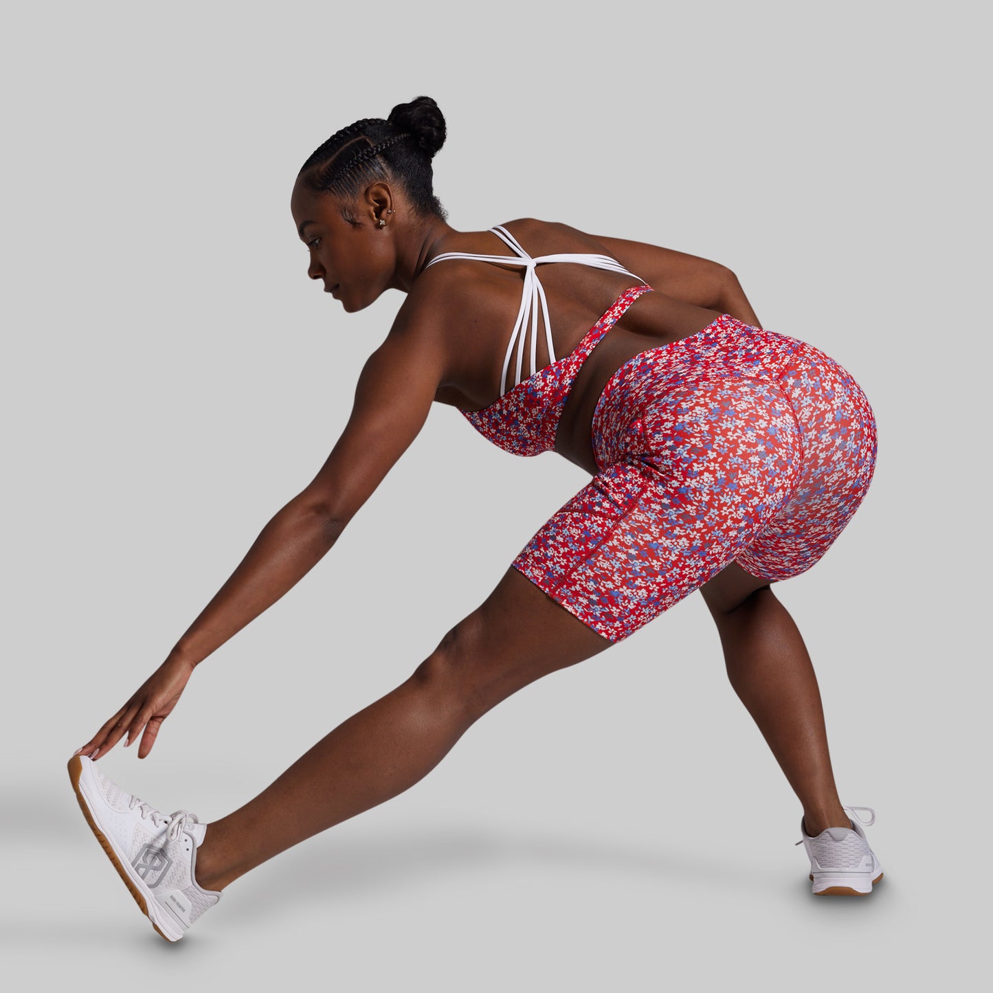 Woman in a floral outfit stretching on a plain background