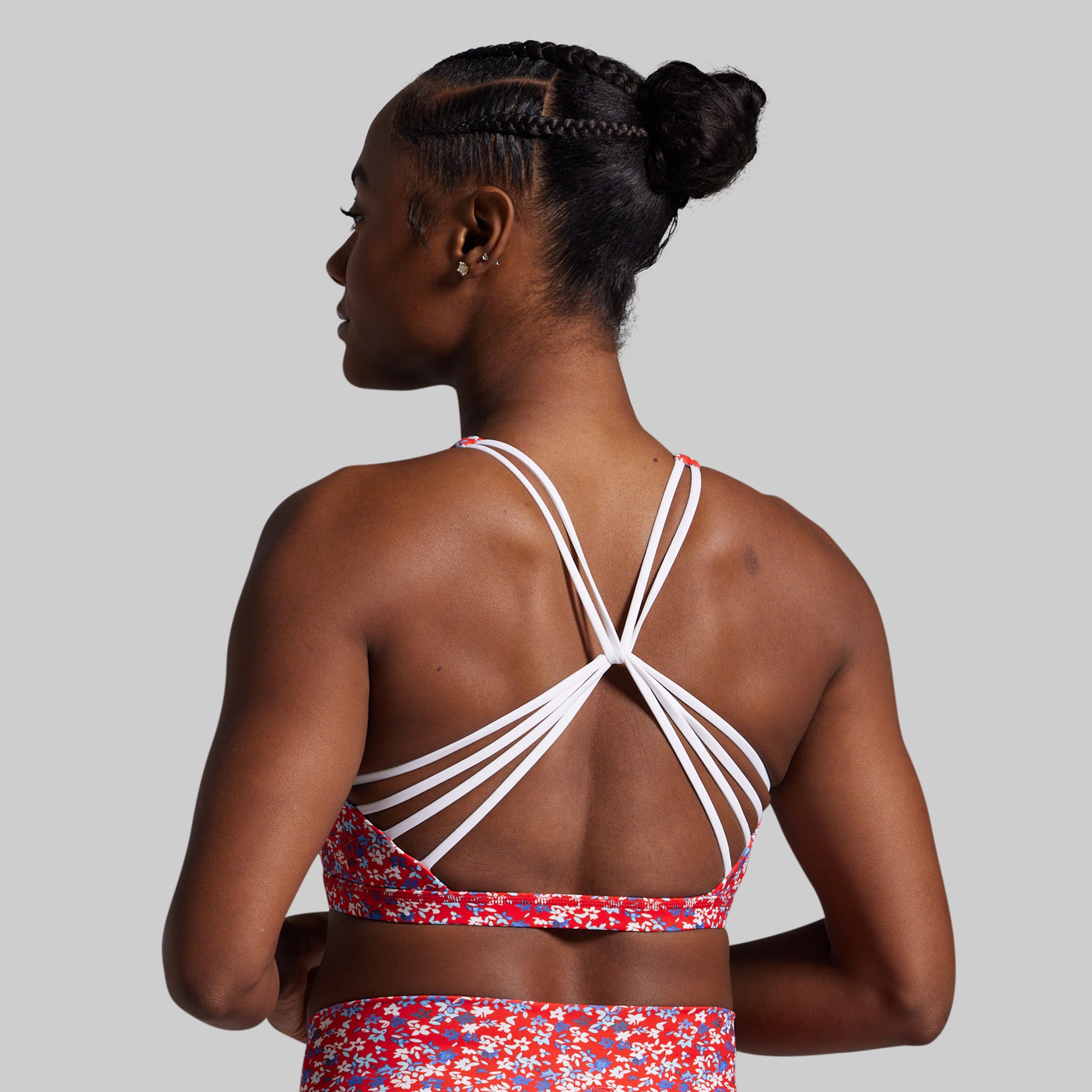 Woman wearing a red and white patterned sports bra and shorts on a gray background