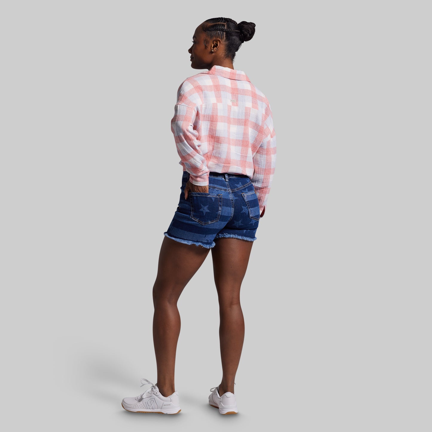 Person wearing a pink plaid shirt and denim shorts on a gray background