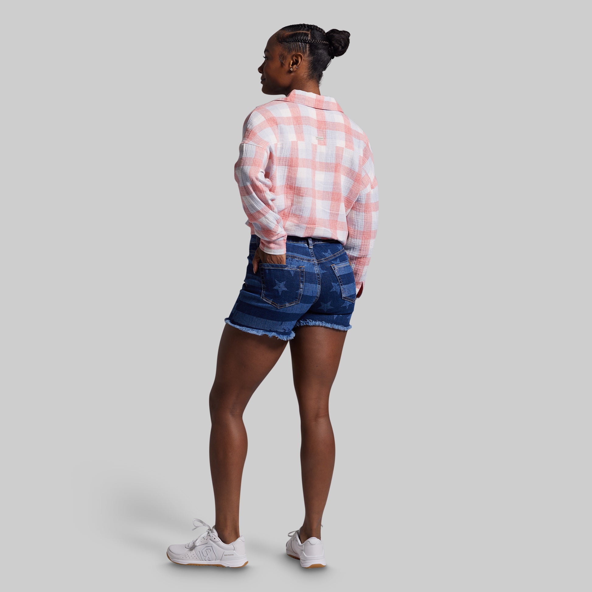 Person wearing a pink plaid shirt and denim shorts on a gray background