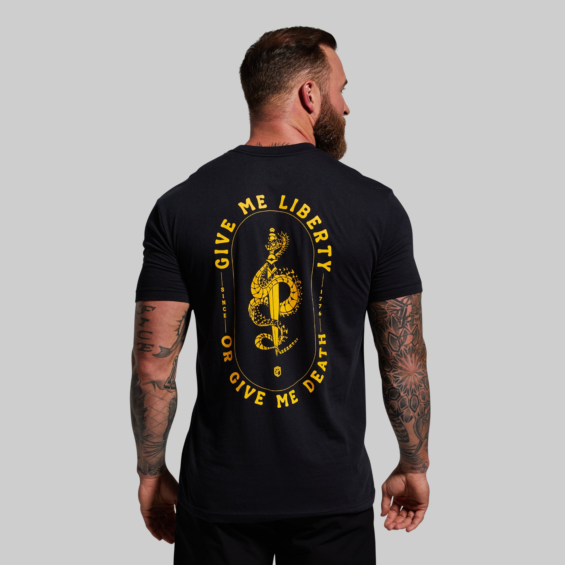 Man wearing a black t-shirt with yellow text and design on the back, standing against a gray background.