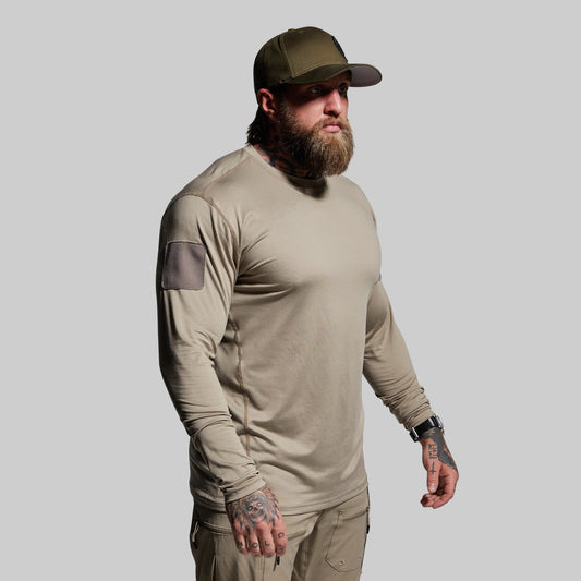 Man wearing a beige long-sleeve shirt and cap on a gray background