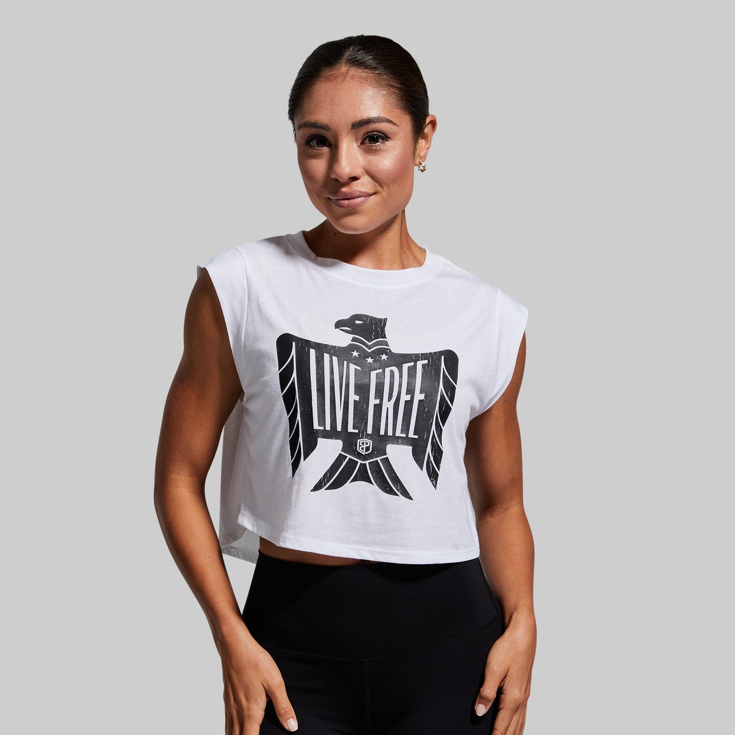 Woman wearing a white sleeveless shirt with 'LIVE FREE' print on a gray background