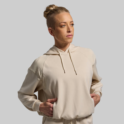 Woman wearing a beige hoodie against a plain background