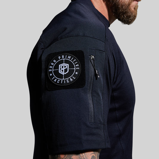 Person wearing a blue tactical shirt with a visible brand patch on the sleeve against a gray background