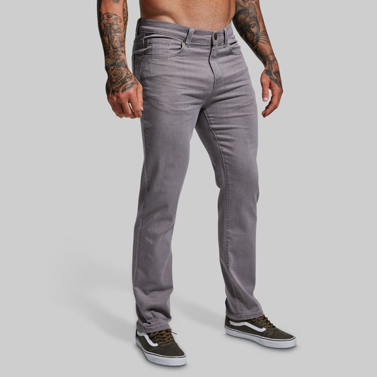 A male model wearing grey stretchy athletic slim fit jeans and black and white sneakers.
