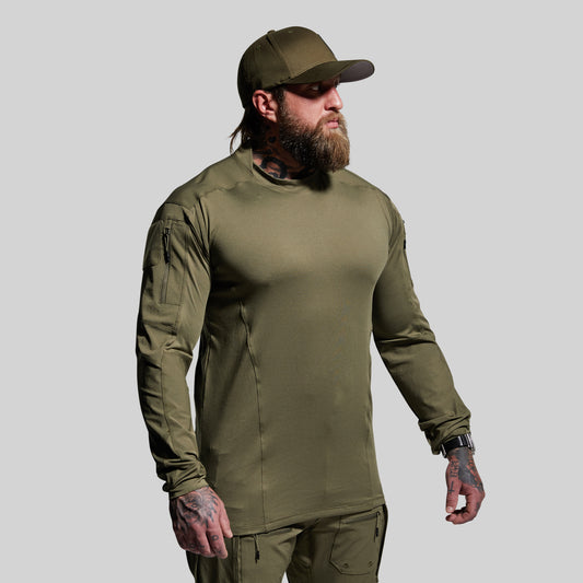 Man wearing an olive green long-sleeve shirt and pants with a cap on a gray background
