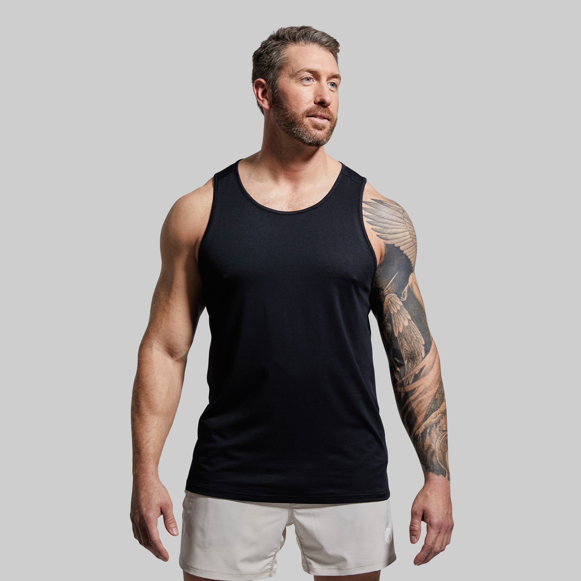 Man wearing a black tank top and white shorts against a gray background
