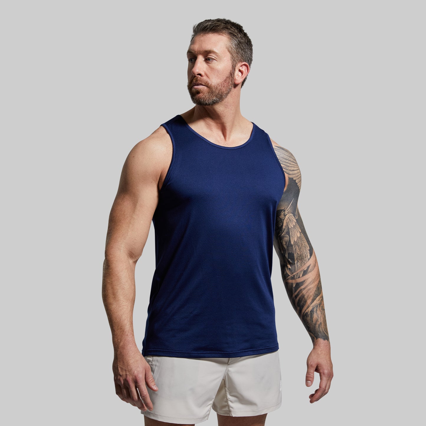 Man wearing a navy tank top and white shorts against a gray background