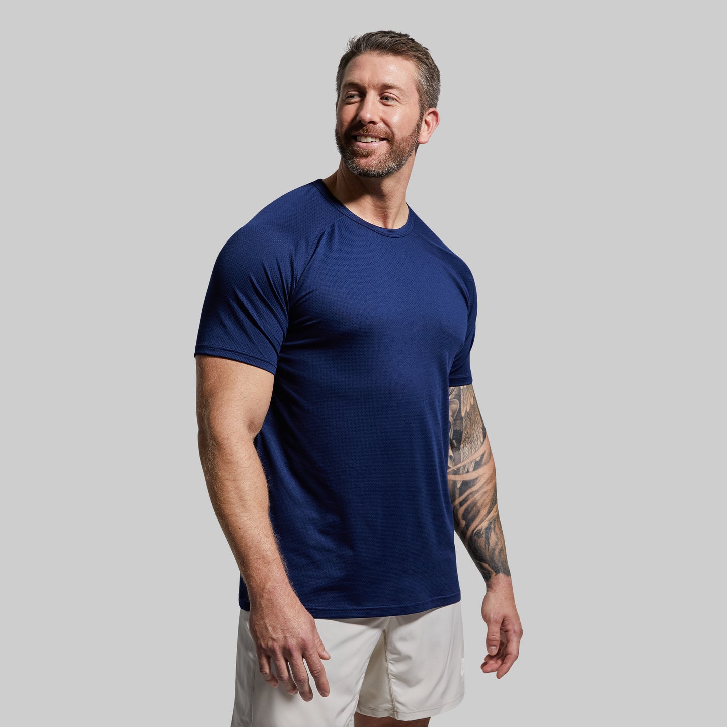 Man wearing a navy blue t-shirt and white shorts against a gray background