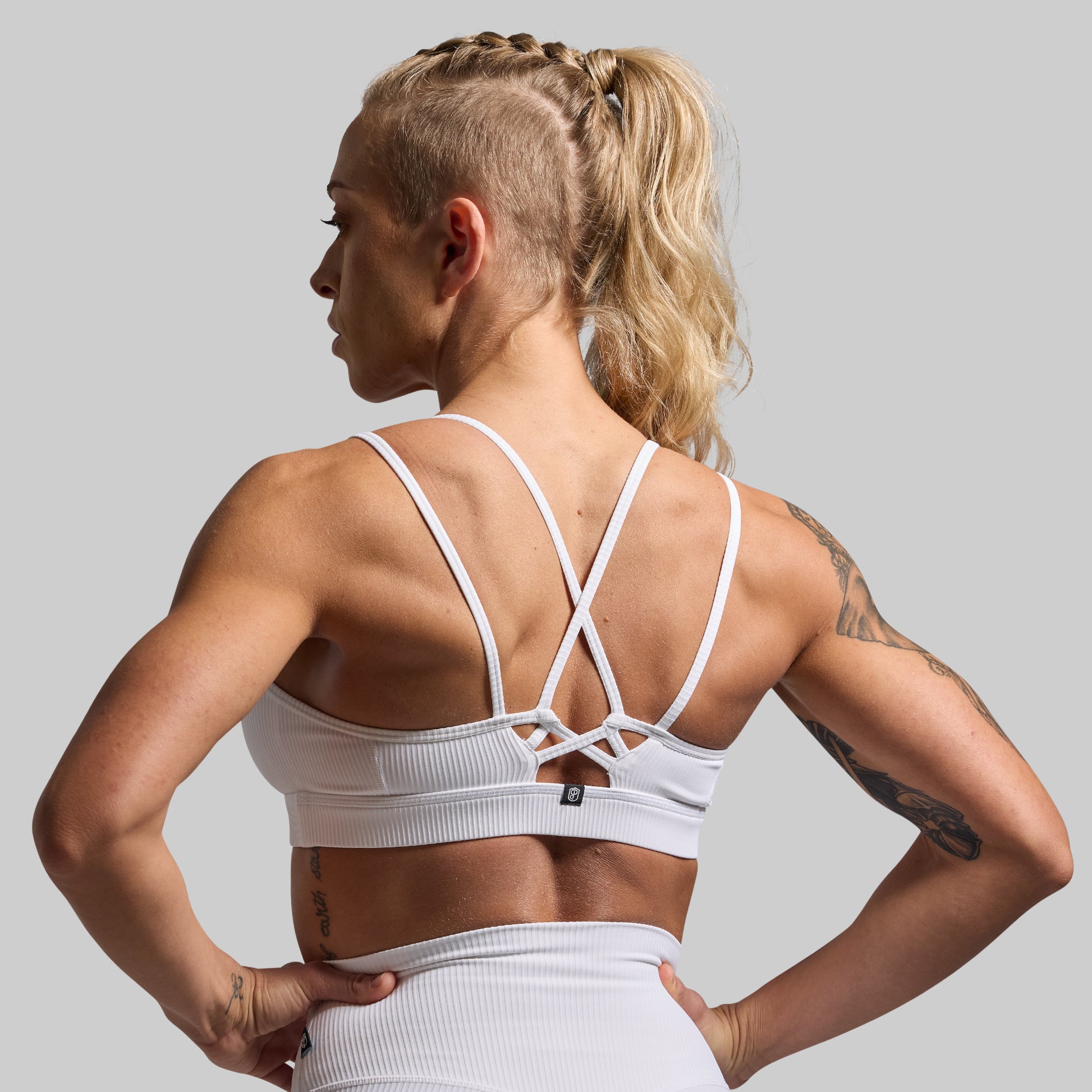 Woman wearing a white sports bra and leggings on a gray background