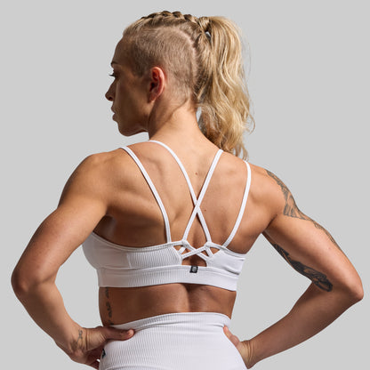 Woman wearing a white sports bra and leggings on a gray background