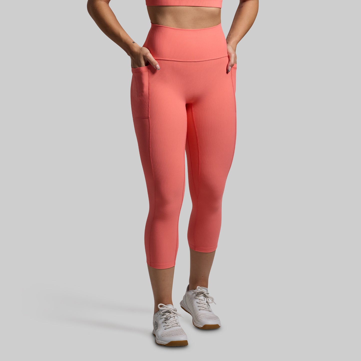 Person wearing coral leggings and white sneakers on a gray background
