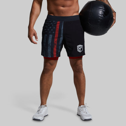 Person wearing black shorts with a flag design, holding a medicine ball on a gray background