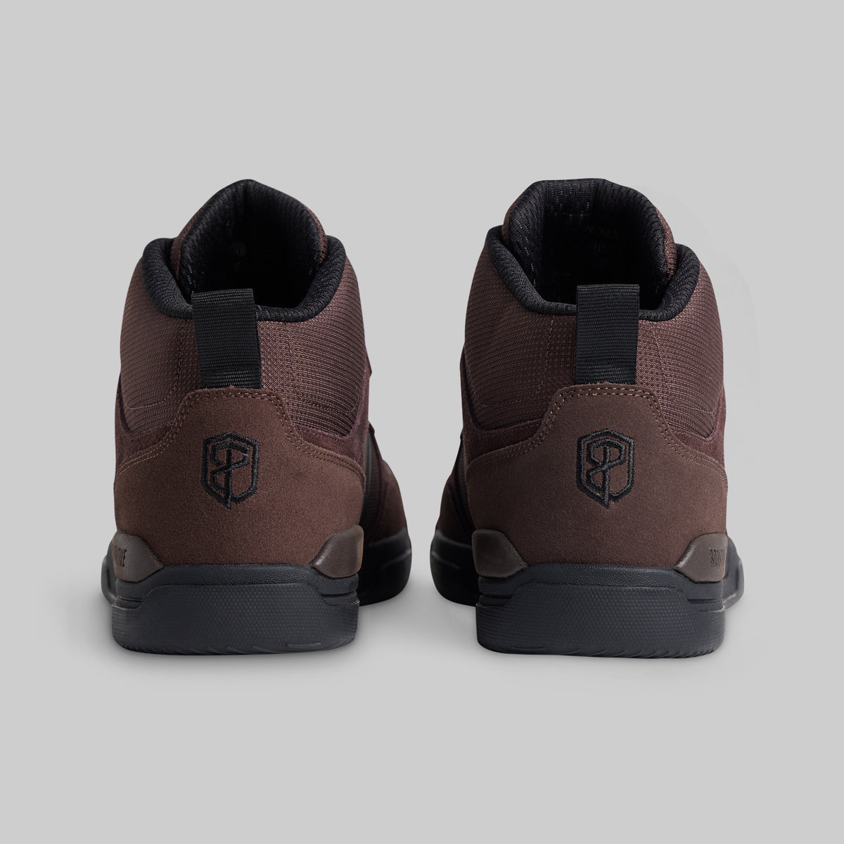 A pair of mid-top athletic shoes shown from the back, featuring a dark brown textured upper, black pull tabs, and black soles on a light gray background.