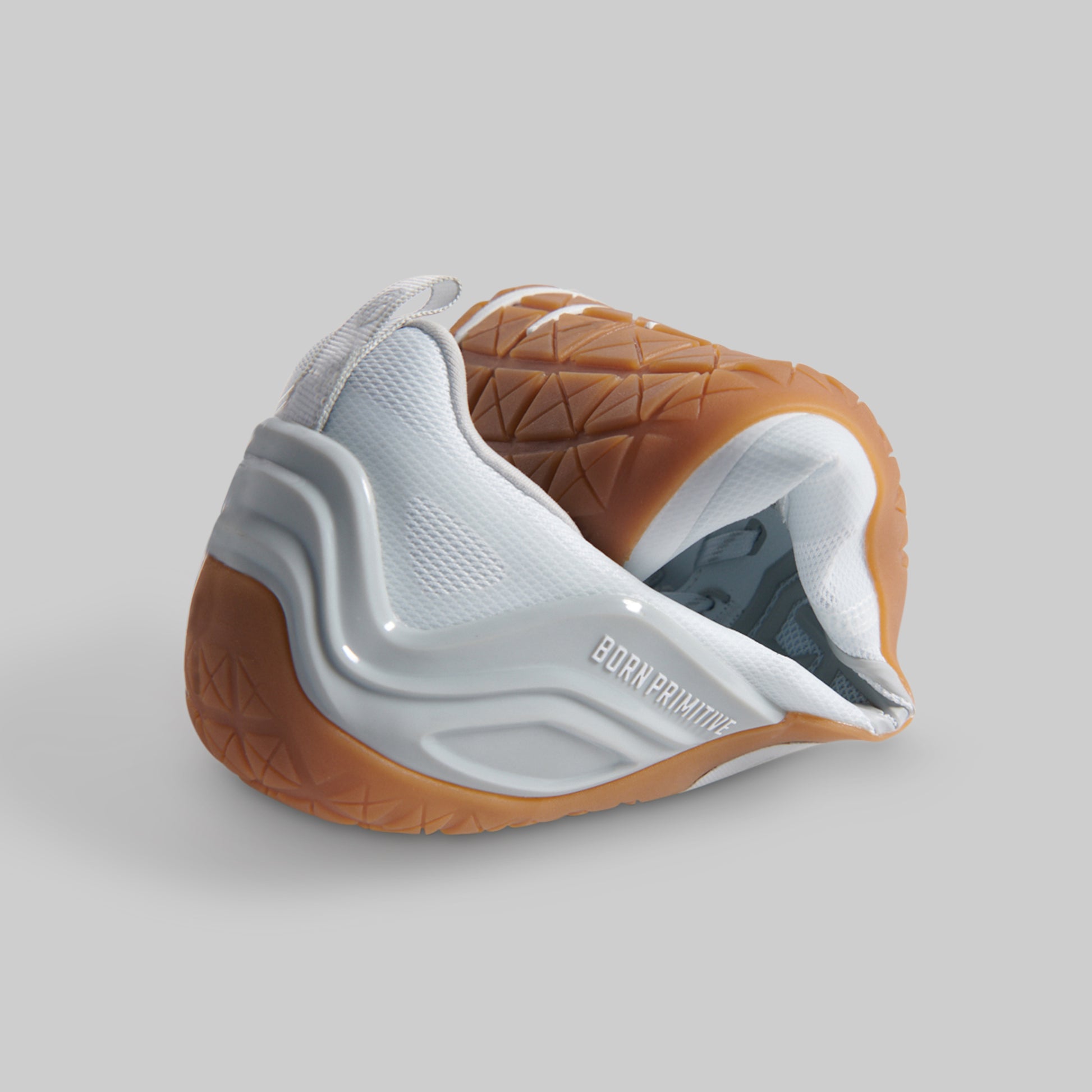 A white and brown athletic barefoot shoe rolled to show flexibility against a solid gray background.