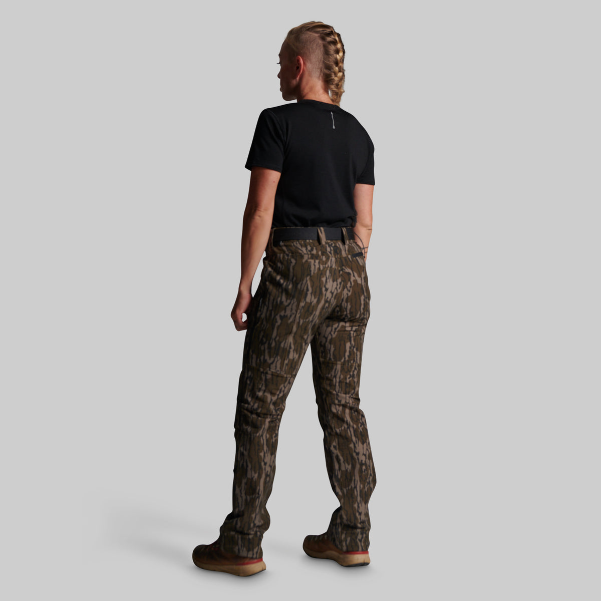 A model shown from the back wearing camouflage cargo pants, a black t-shirt, and brown boots against a solid gray background.