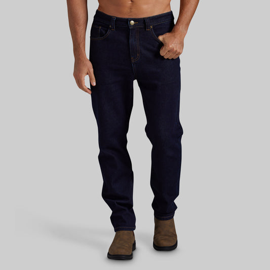 A man wearing dark navy blue slim-fit jeans and brown boots, shown from the waist down against a solid gray background.