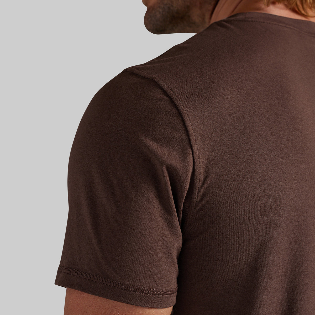 Close-up of a man wearing a dark brown short-sleeve crewneck t-shirt, showing the back and shoulder area against a light gray background.