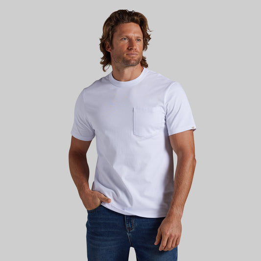 A man wearing a white short-sleeve crewneck pocket t-shirt and blue jeans, standing against a solid gray studio background.