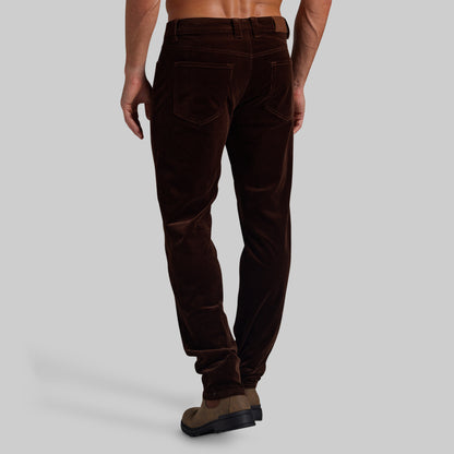 A man wearing dark brown corduroy trousers, shown from a rear three-quarter angle against a solid light gray background.