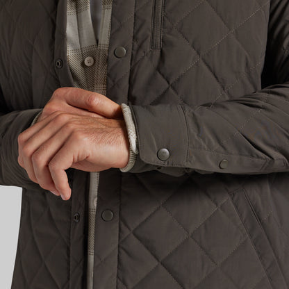 Close-up of a person wearing a dark grey diamond-quilted jacket, showing the quilted texture, snap-button closure, and a plaid shirt underneath.