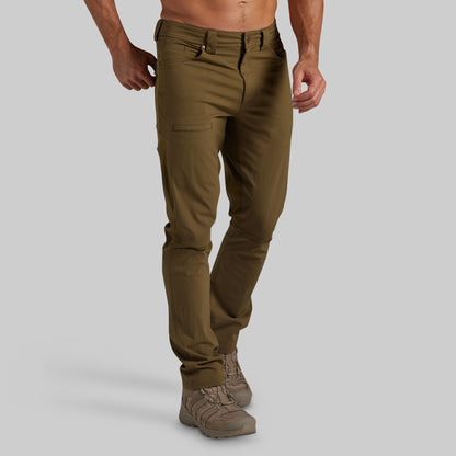 A man wearing olive green pants and brown hiking boots, shown from the waist down against a solid gray background.