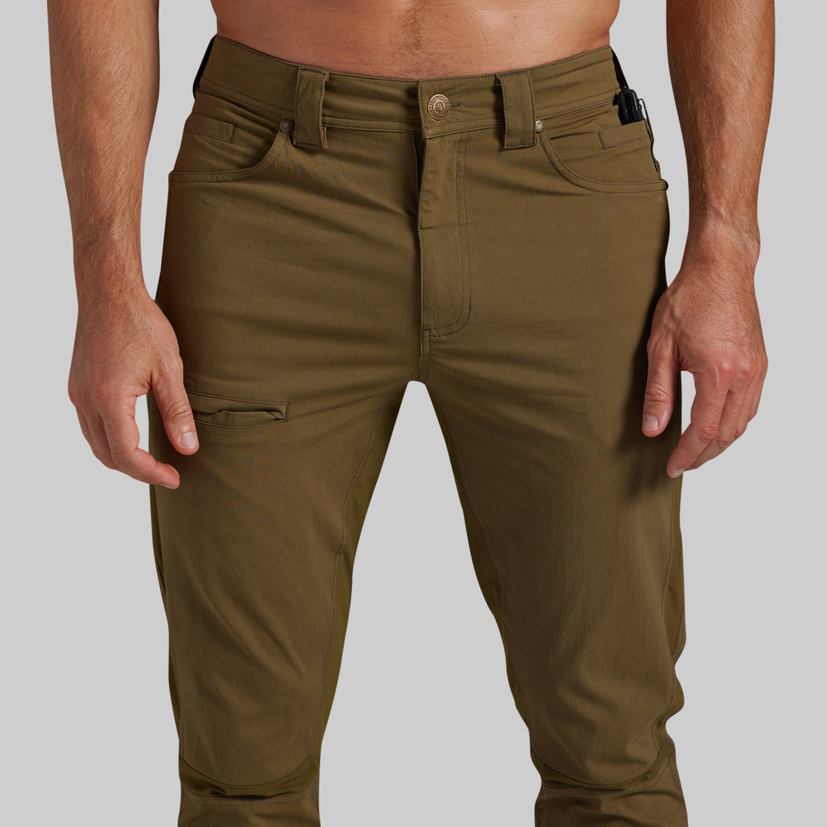 A close-up of a person wearing olive green cargo-style pants against a light gray studio background.