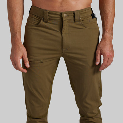 A close-up of a person wearing olive green cargo-style pants against a light gray studio background.
