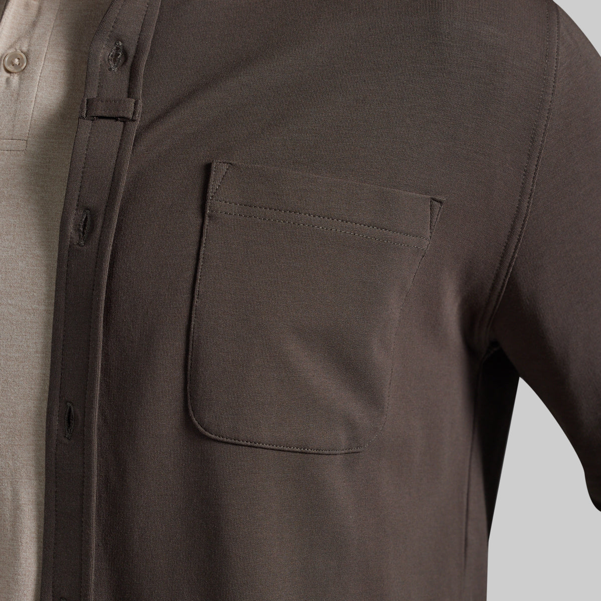 Close-up of a dark olive brown overshirt worn over a light beige polo shirt, highlighting chest pocket