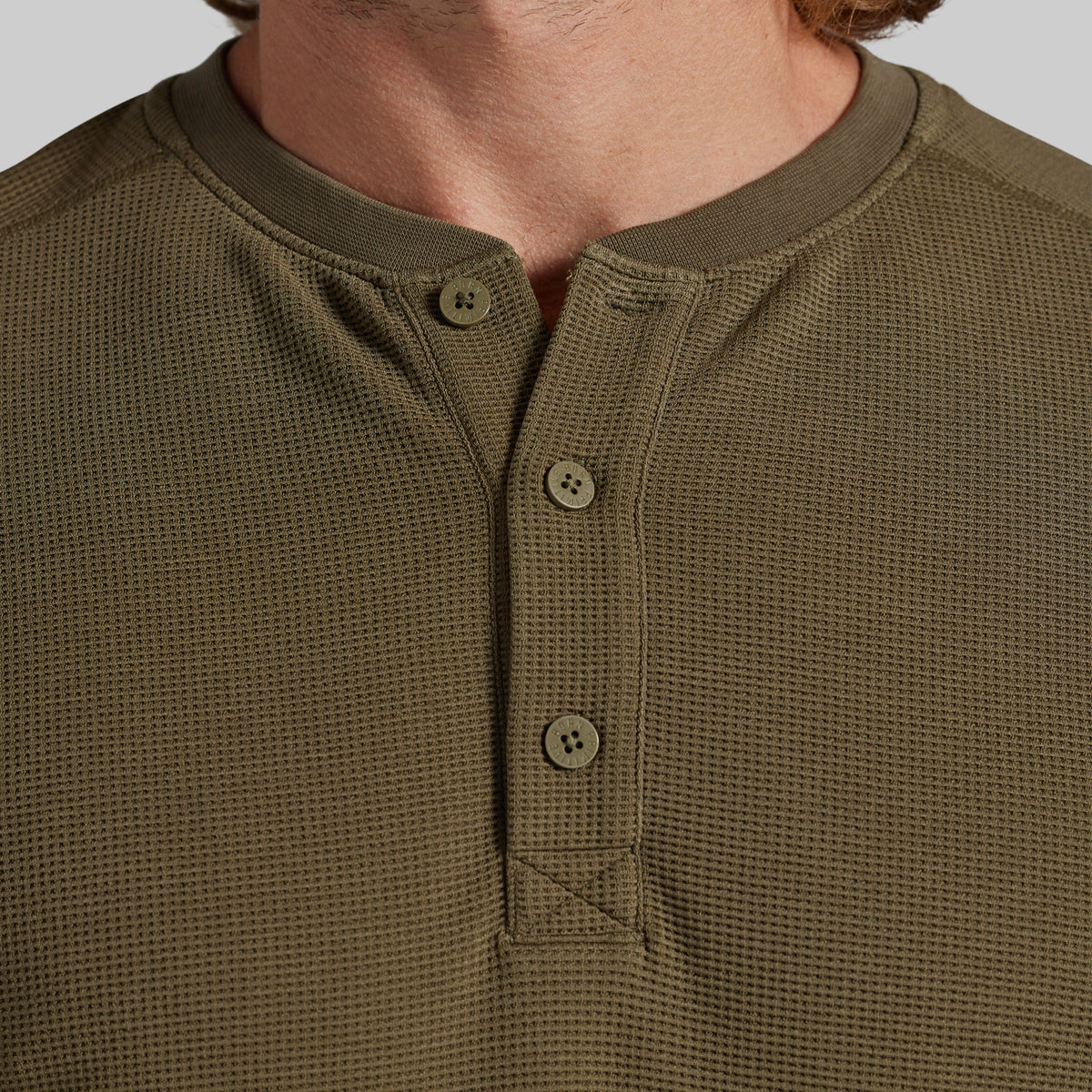 Close-up of a man wearing an olive green waffle-knit henley shirt with a three-button placket.