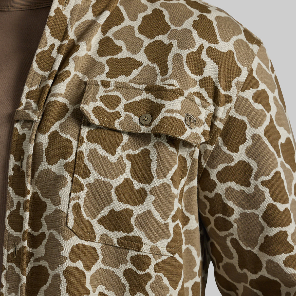 Close-up of a brown and beige frog camo shirt jacket with a chest pocket and button closure.