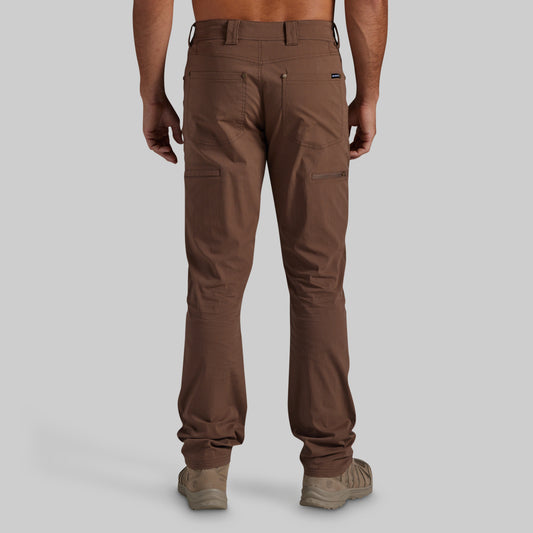 A man shown from the back wearing brown cargo pants and tan hiking boots against a solid gray studio background.