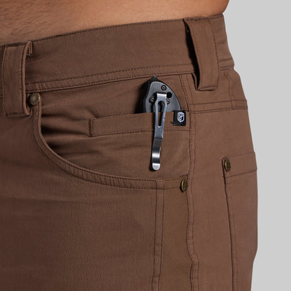 Close-up of a person wearing brown pants, showing the back pocket with a black metal pocket clip holding a small black accessory.