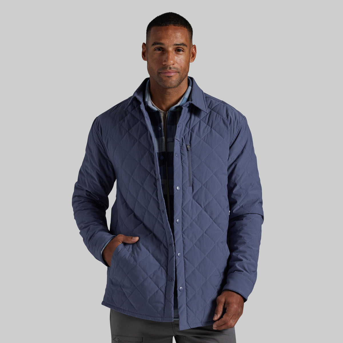 A man wearing a navy blue diamond-quilted button-up jacket over a dark plaid shirt, photographed against a solid light gray background.