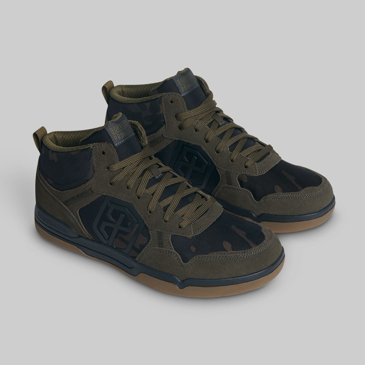 A pair of mid-top sneakers in olive green and black with a subtle camouflage pattern, featuring gum soles, set against a solid gray background.