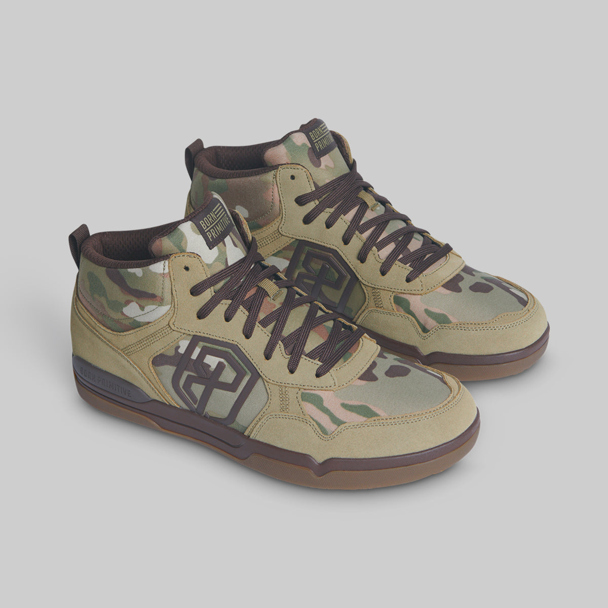 A pair of mid-top sneakers in a camouflage pattern with tan, green, and brown tones, featuring dark brown laces and soles, shown on a solid gray background.