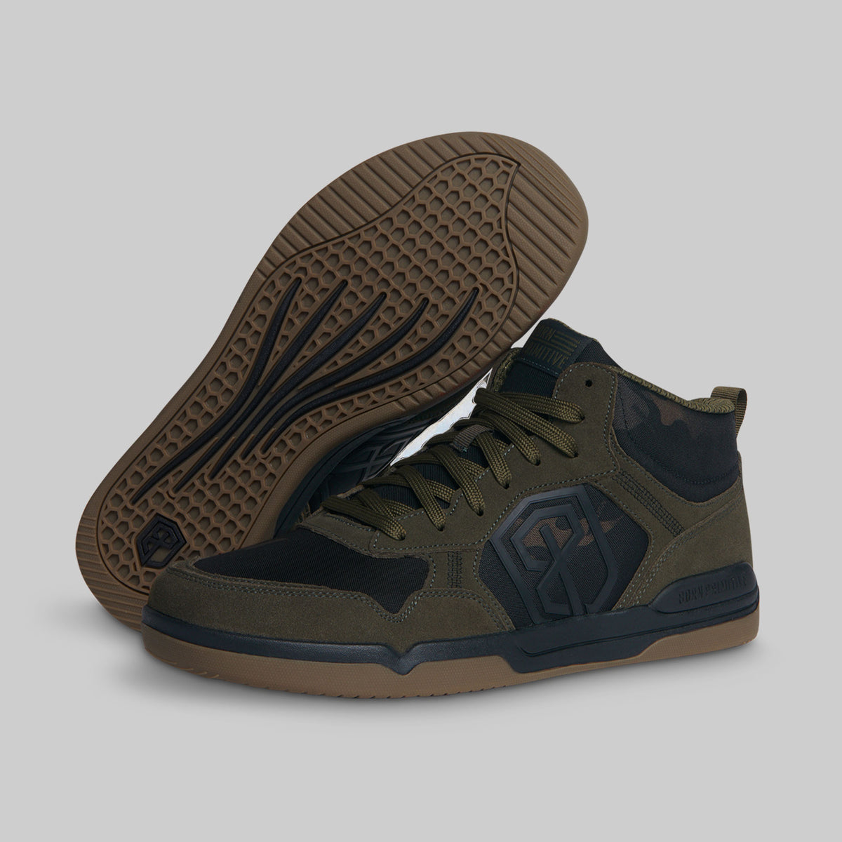 A pair of mid-top sneakers in olive green and black, with one shoe standing upright and the other tilted to show the textured brown outsole, set against a solid gray background.