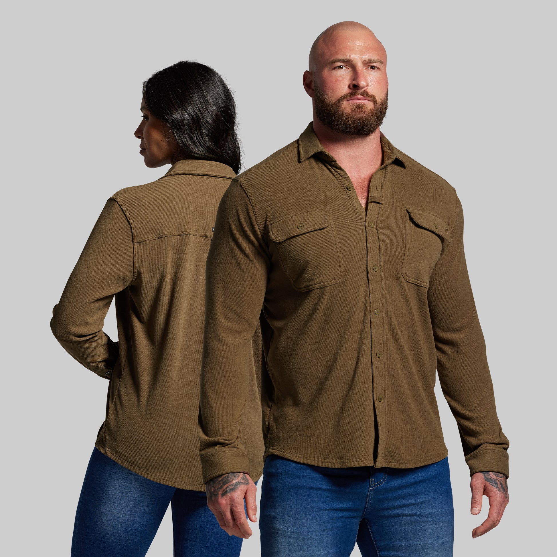 Two people wearing brown shirts and blue jeans against a gray background