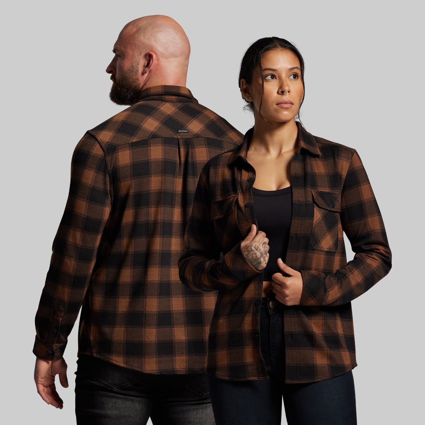 Two people wearing brown plaid shirts against a gray background