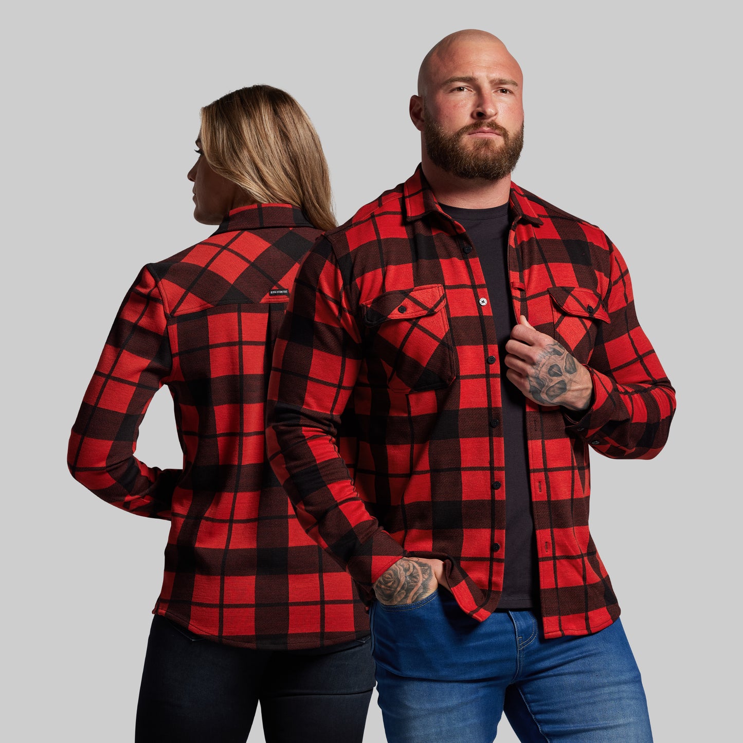 Two people wearing red and black plaid shirts against a gray background