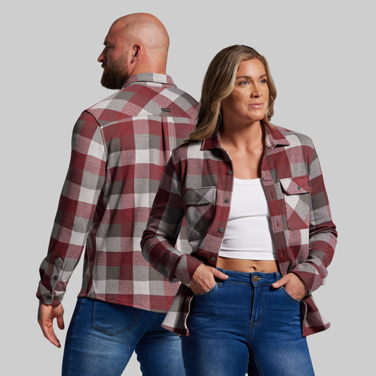 Man and woman wearing matching plaid shirts and jeans on a gray background