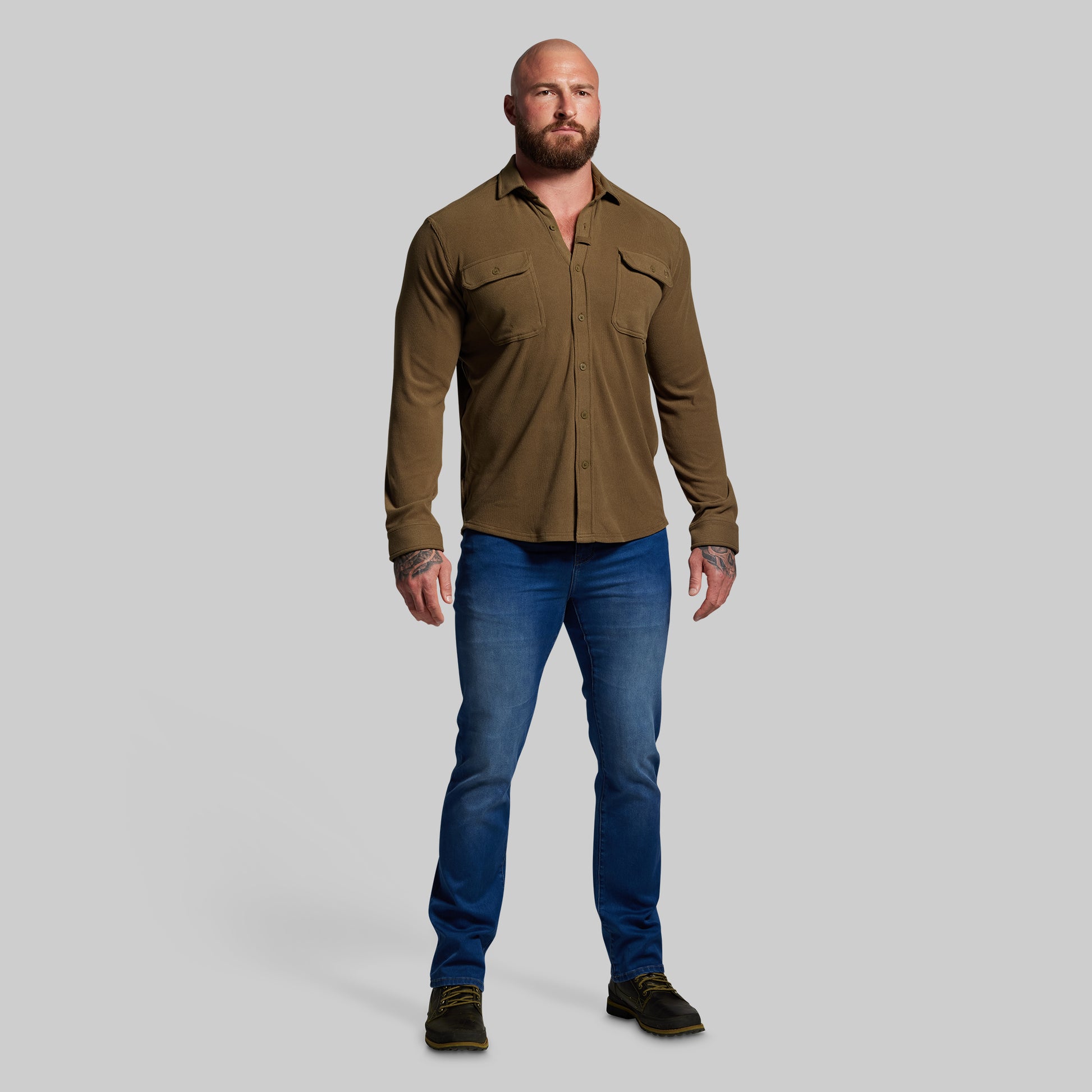 Man wearing a brown shirt and blue jeans on a gray background