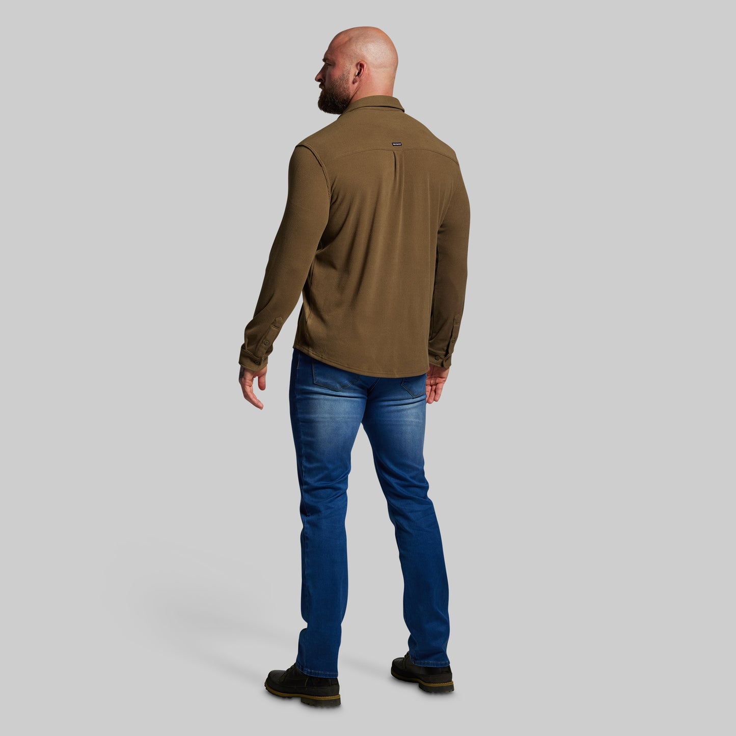 Man wearing a brown shirt and blue jeans on a gray background