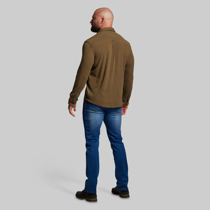 Man wearing a brown shirt and blue jeans on a gray background