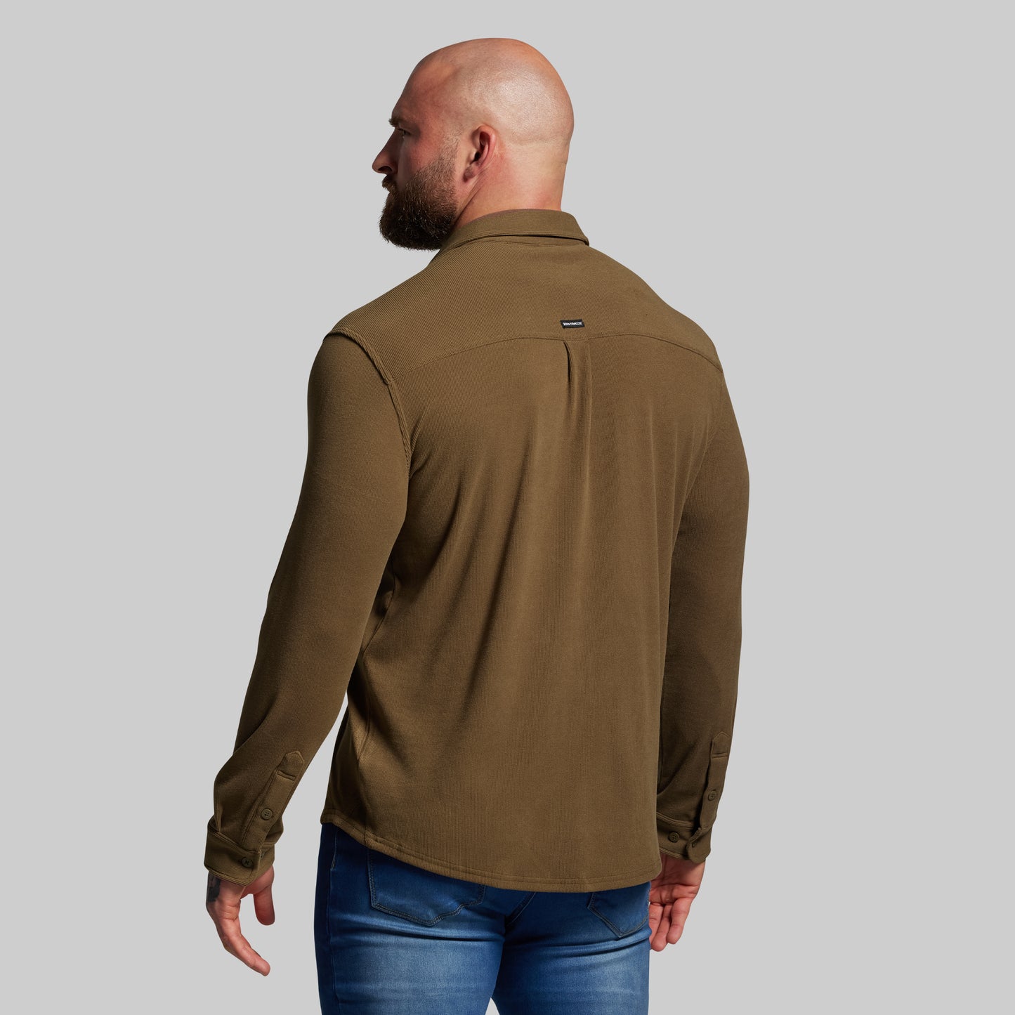 Man wearing a brown shirt and blue jeans on a gray background