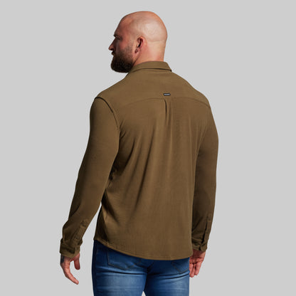 Man wearing a brown shirt and blue jeans on a gray background