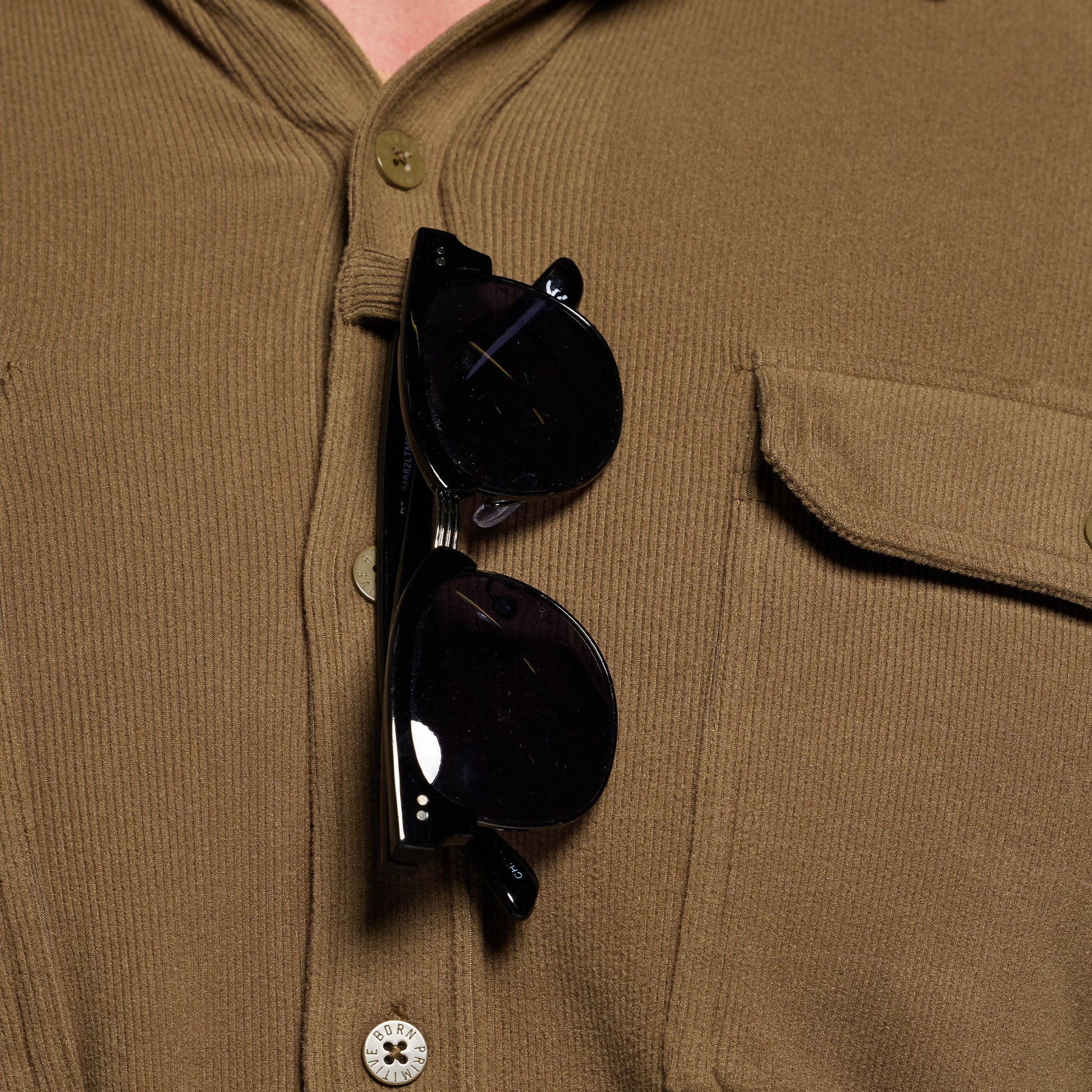 Black sunglasses hanging on a brown corduroy shirt with buttons